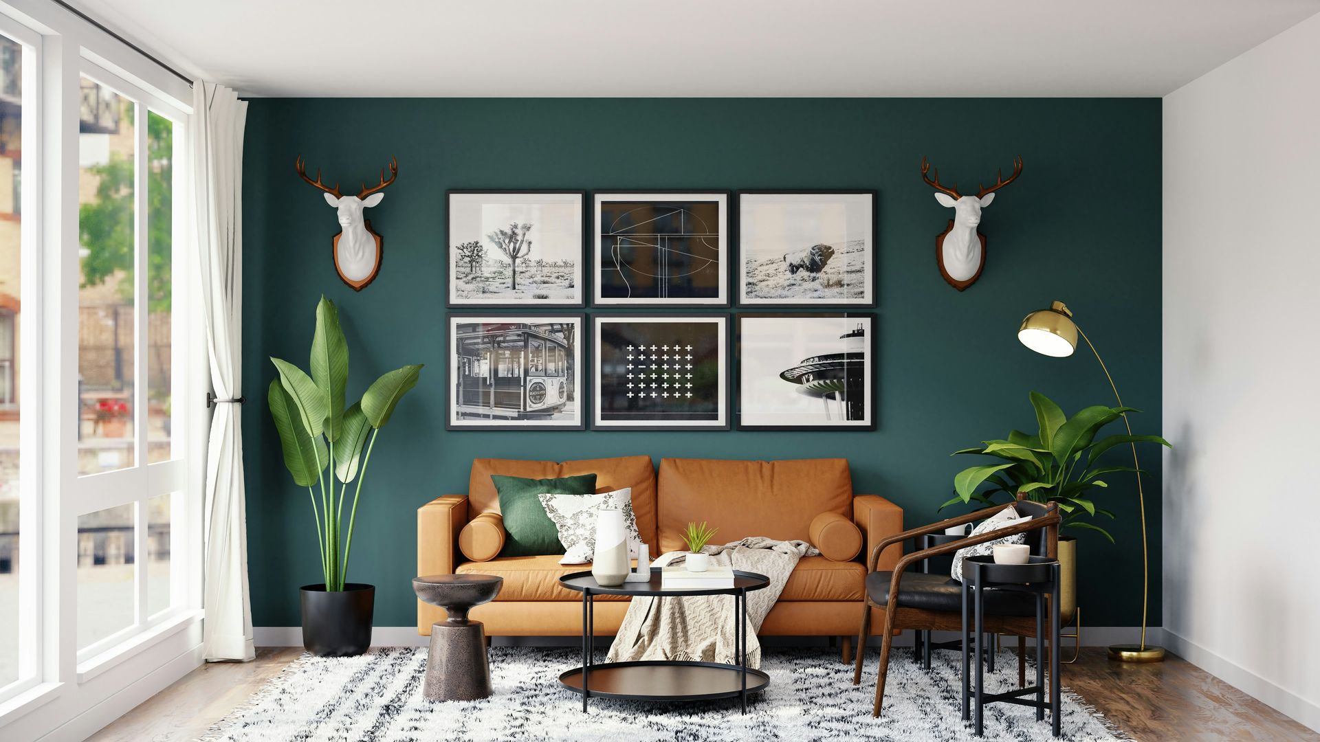 A tan leather sofa against a dark green wall with framed art and deer heads
